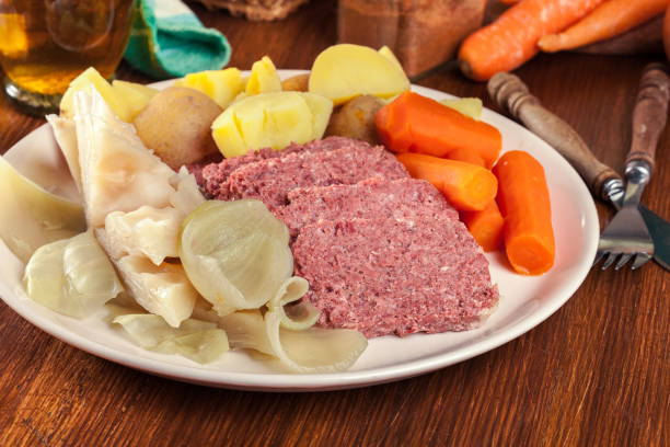 A plate of hearty food including sliced meat, potatoes, carrots, and cabbage on a wooden table.