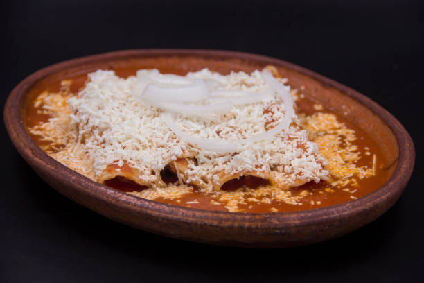 A delicious plate of enchiladas topped with cheese and onions in a brown ceramic dish.