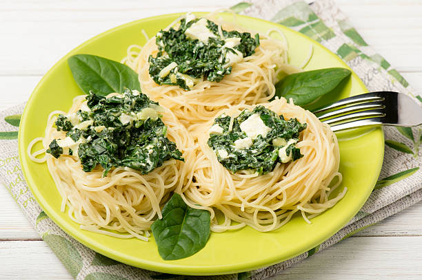 A plate of spaghetti topped with green spinach and creamy sauce, garnished with fresh spinach leaves.