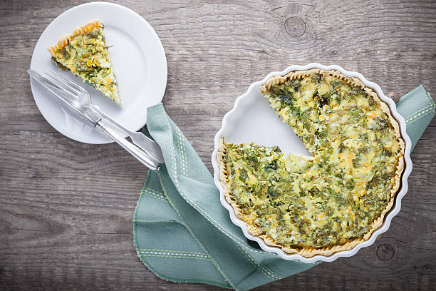 A delicious herb quiche with a slice removed, presented on a wooden table with a plate and fork.