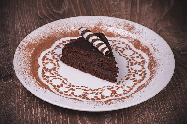 A slice of chocolate cake on a decorative plate with cocoa powder design.