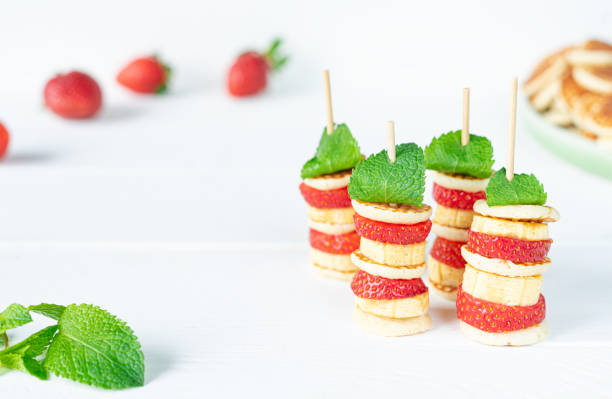 A creative arrangement of banana and strawberry stacks topped with mint leaves on wooden skewers.