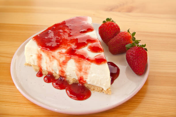 A slice of cheesecake topped with strawberry sauce and accompanied by fresh strawberries on a white plate.