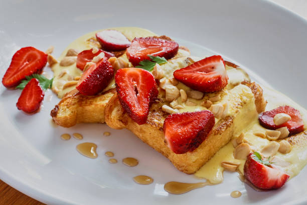 Delicious French toast topped with fresh strawberries, peanuts, and a drizzle of syrup on a white plate.