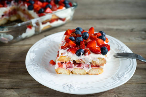 A slice of layered dessert with strawberries and blueberries on top, served on a white plate.