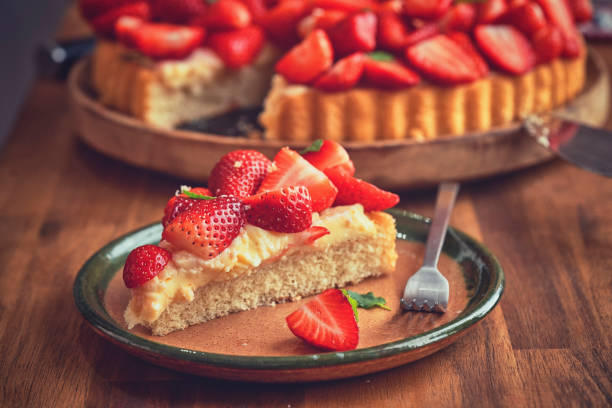 A slice of strawberry cake on a green plate with a fork, next to a whole cake topped with fresh strawberries.