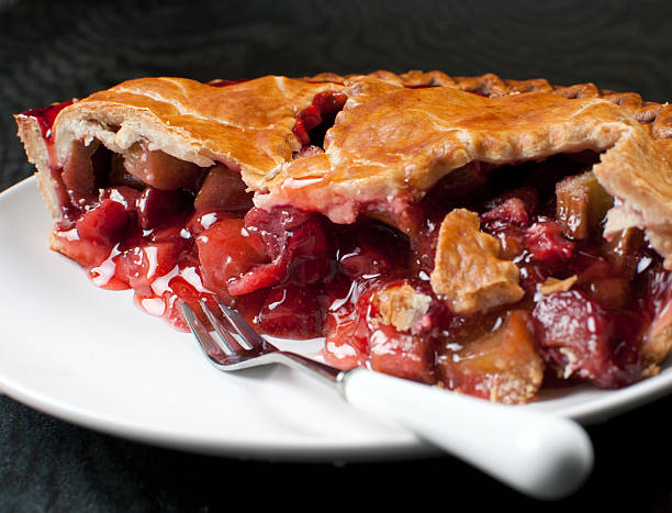 A slice of cherry apple pie on a plate, with fruit filling spilling out.