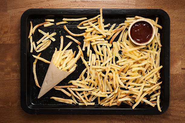 Plate of crispy French fries with a paper cone filled with fries and a small bowl of ketchup on a wooden table.