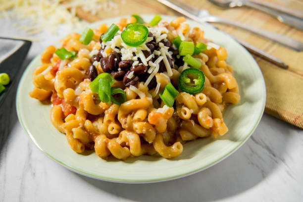 A plate of macaroni mixed with black beans, topped with grated cheese, sliced jalapeños, and chopped green onions.