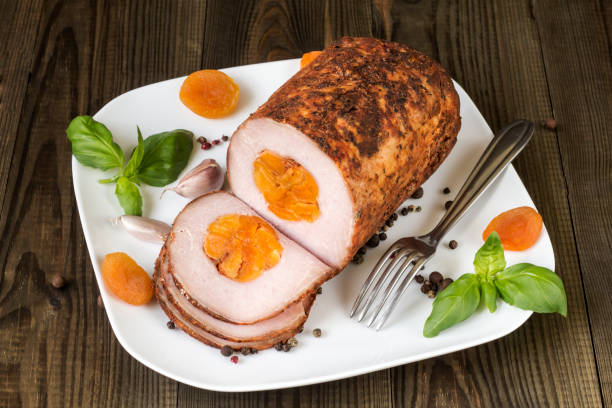 A sliced loaf of meat with apricots and herbs on a white plate.