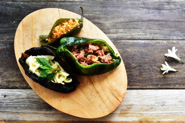 Three stuffed peppers on a wooden board, showcasing a variety of fillings.