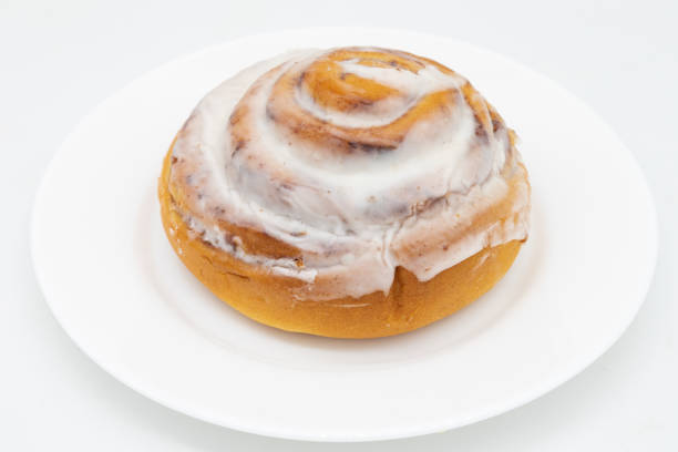 A freshly baked cinnamon roll topped with creamy icing on a white plate.