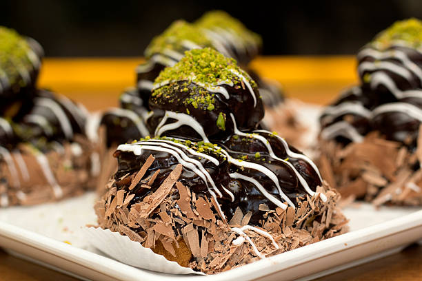 Close-up of decorative chocolate desserts topped with green pistachio pieces and white icing on a plate.