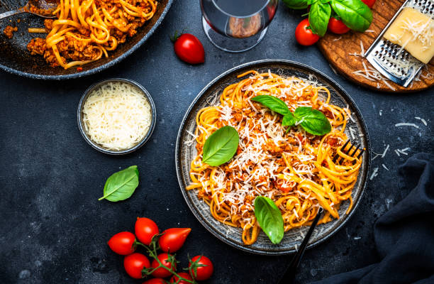 A delicious plate of spaghetti topped with basil and grated cheese, accompanied by cherry tomatoes and a glass of water.