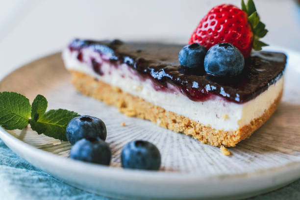 A slice of cheesecake topped with jelly, blueberries, and a strawberry on a beige plate.