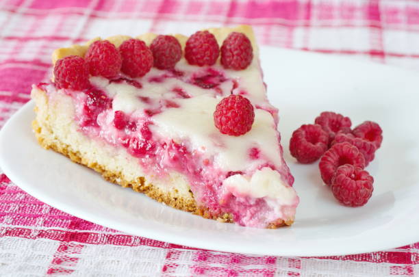 A slice of raspberry cheesecake on a white plate, garnished with fresh raspberries.