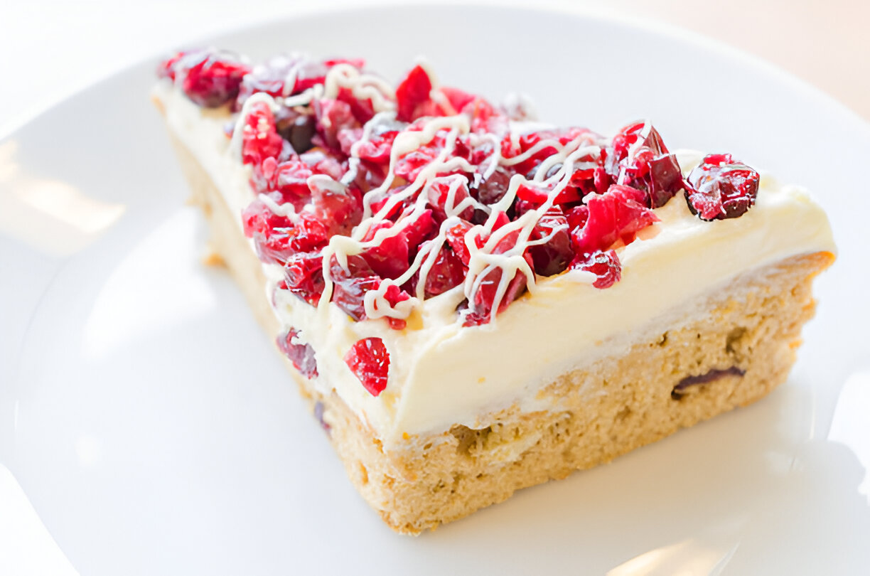 A slice of dessert topped with red berries and drizzled with white chocolate on a plate.