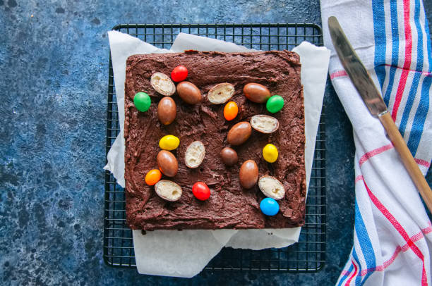 A fudgy chocolate brownie topped with colorful candy eggs arranged in a circular pattern on a cooling rack.