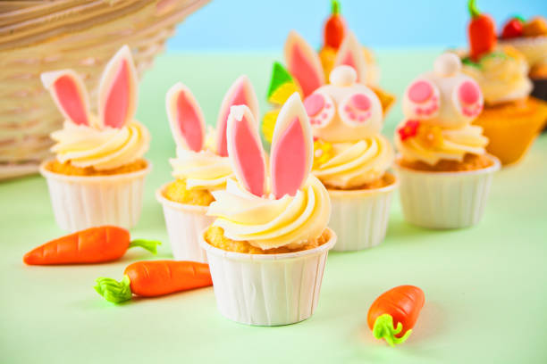 Colorful cupcakes decorated with bunny ears and small carrots on a pastel background.