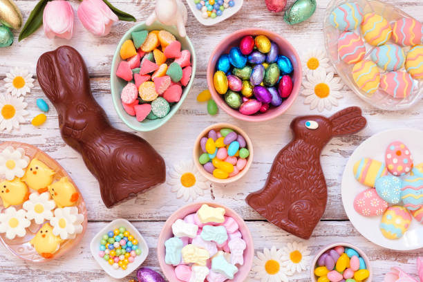 A festive spread of colorful Easter candies and decorations including chocolate bunnies, pastel eggs, and floral accents.