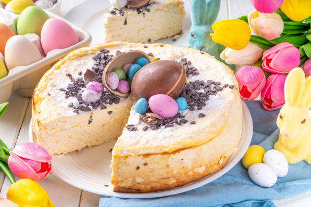 A beautifully decorated cheesecake with chocolate and colorful Easter eggs on top, surrounded by spring flowers and festive decorations.