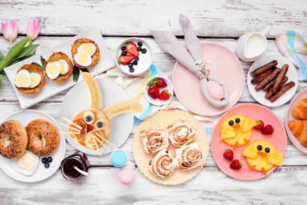 A colorful breakfast spread featuring fun, themed foods, including a bunny-shaped pancake, pastries, fruits, and beverages, arranged on a rustic wooden table.