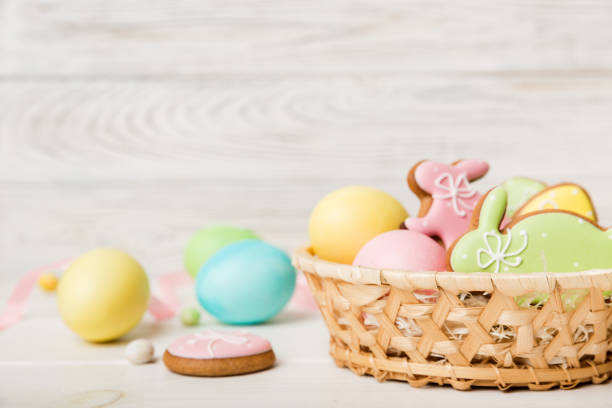 A woven basket filled with colorful Easter eggs and decorated cookies on a light wooden background.