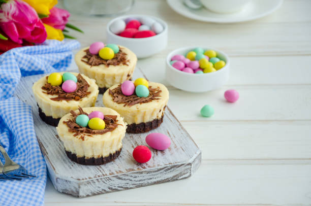 Mini cheesecake desserts with chocolate shavings and colorful candy eggs on a wooden serving board.