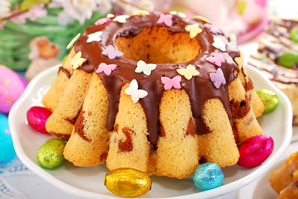 A beautifully decorated cake topped with chocolate icing and colorful candy butterflies, surrounded by shiny chocolate eggs.