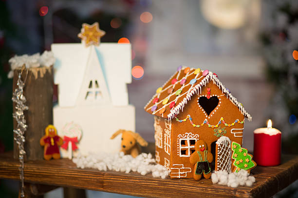 A festive display featuring a gingerbread house, a white house, and decorative figures including a dog and a gingerbread man, with a lit candle nearby.