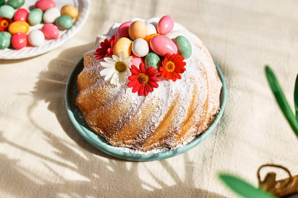 A decorative bundt cake topped with colorful candy eggs and flowers, situated on a green plate with a soft background.