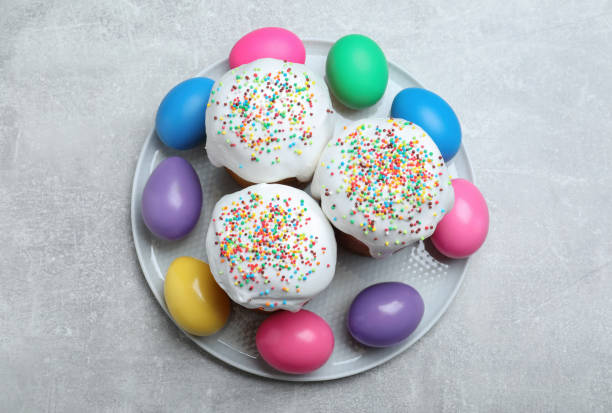 A plate with two frosted cupcakes topped with colorful sprinkles surrounded by pastel-colored eggs.