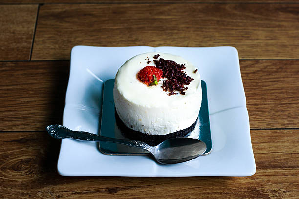 A delicious cheesecake topped with a strawberry and chocolate shavings on a square plate.