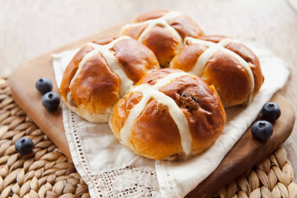 Four freshly baked hot cross buns on a wooden board with blueberries.