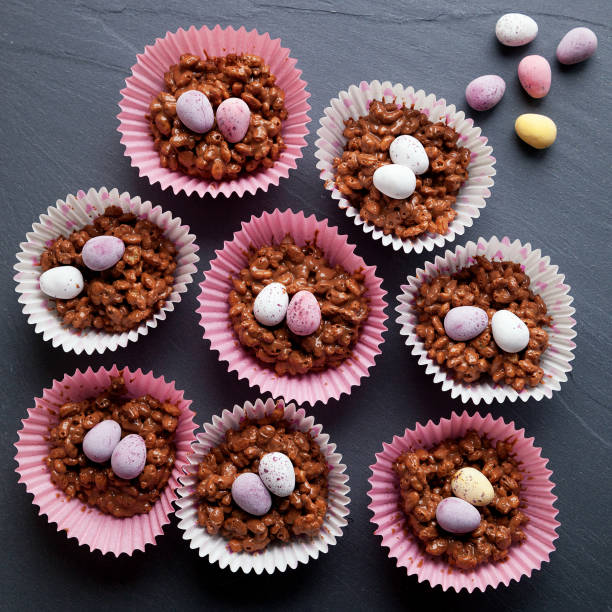 Colorful chocolate nests with candy eggs in pink paper cups on a dark surface.