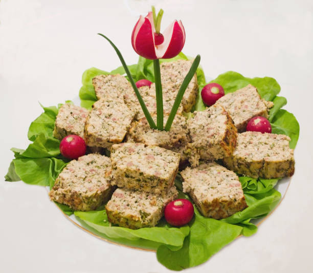 A platter of layered meat dish garnished with lettuce, radishes, and a decorative flower.