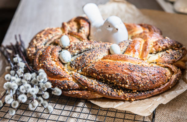 A beautifully braided pastry topped with poppy seeds and decorated with small white eggs and a ceramic bird, alongside soft, fluffy branches.