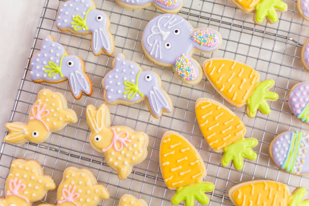 A variety of beautifully decorated Easter cookies shaped like bunnies and pineapples displayed on a cooling rack.