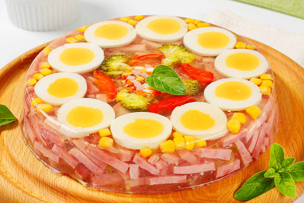 A colorful jellied dish with sliced boiled eggs, ham, and vegetables displayed on a wooden platter.