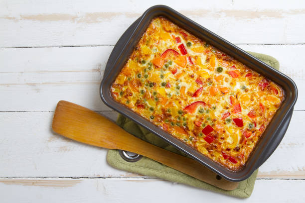 Baked vegetable casserole in a grey baking dish on a wooden surface with a wooden spatula beside it.