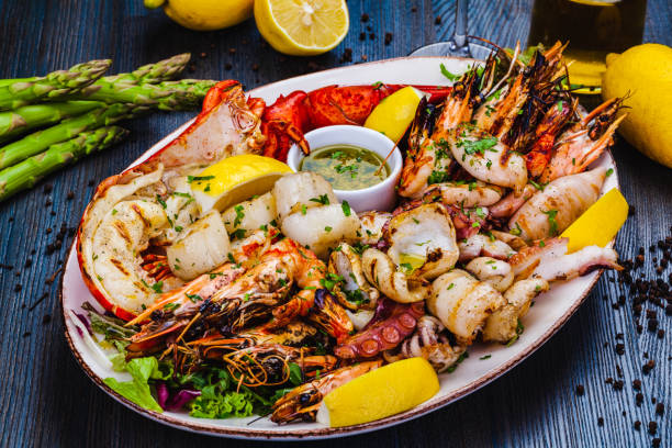 A beautifully arranged platter of grilled seafood, including shrimp, lobster, squid, scallops, and garnished with lemon and herbs.