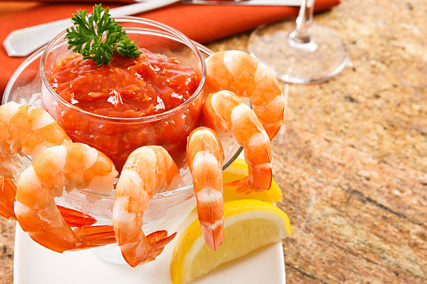 A glass bowl filled with shrimp cocktail served with lemon slices and garnished with parsley.