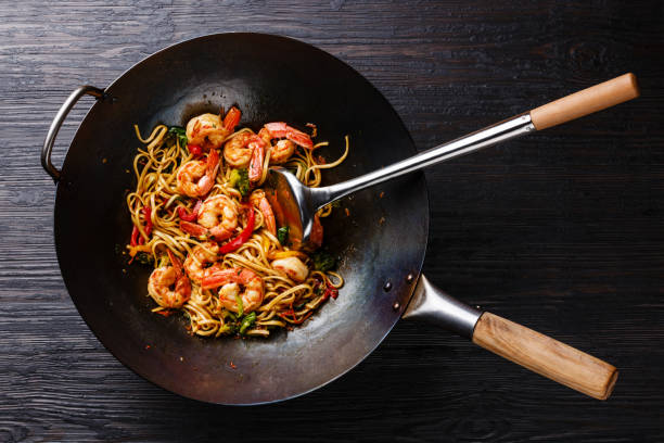 Stir-fried shrimp and vegetables with noodles in a black wok on a dark wooden surface.