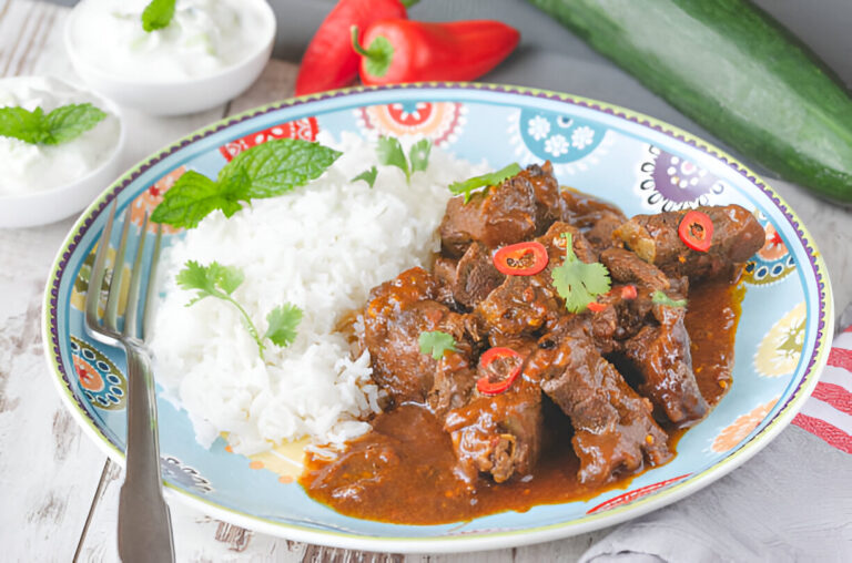 A colorful plate of beef curry served with white rice, garnished with cilantro and sliced red chilies.