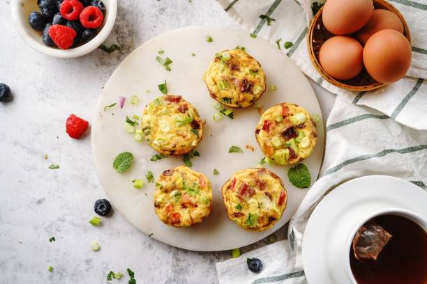 Delicious mini egg muffins arranged on a plate with fresh berries and eggs in the background.