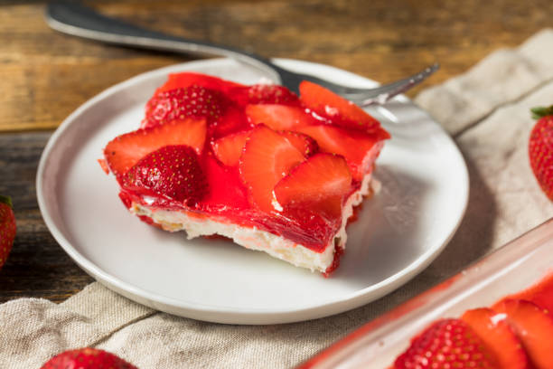 A slice of strawberry dessert on a white plate with fresh strawberries beside it