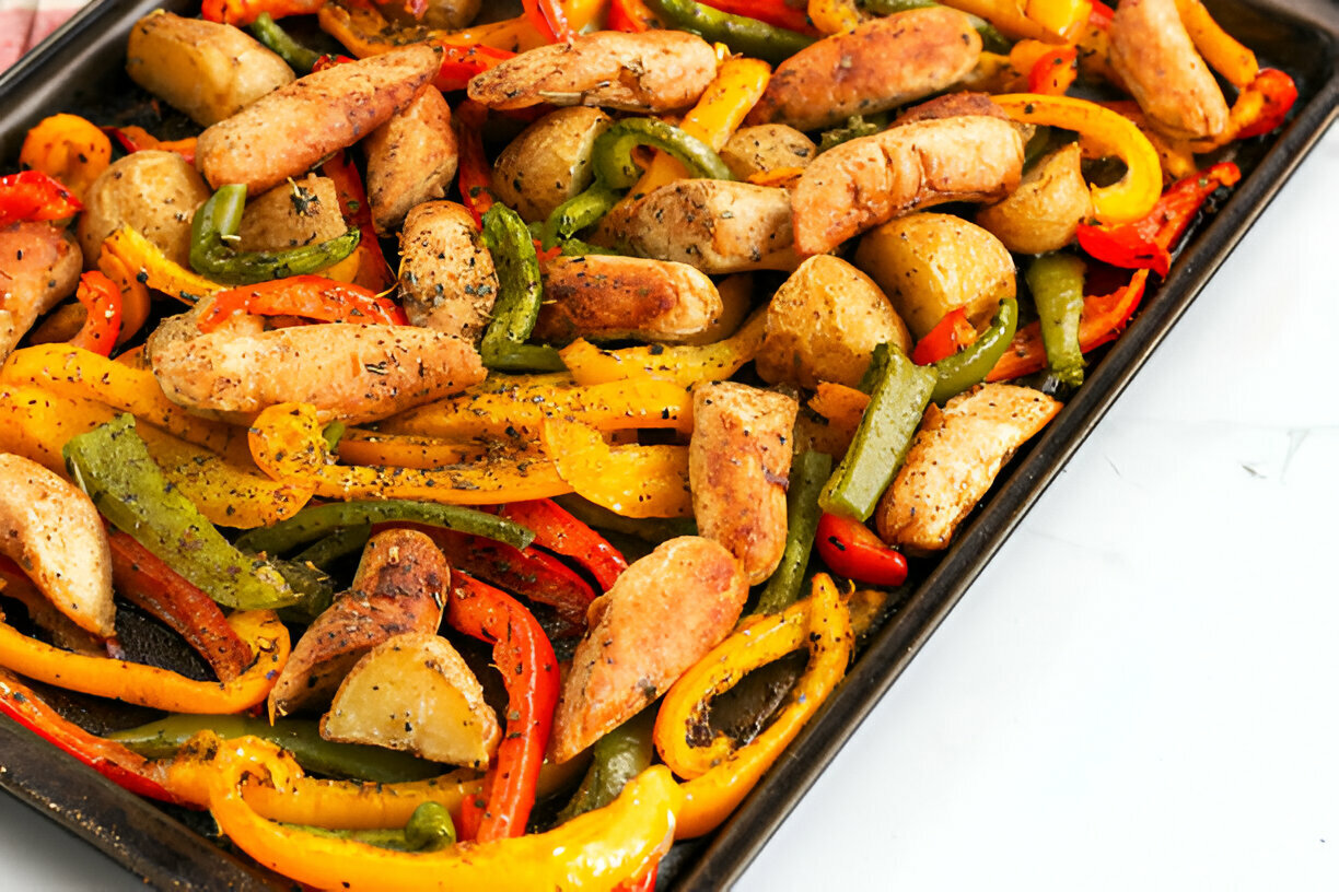 A vibrant tray of roasted vegetables and chicken sausages, featuring bell peppers, baby potatoes, and spices.