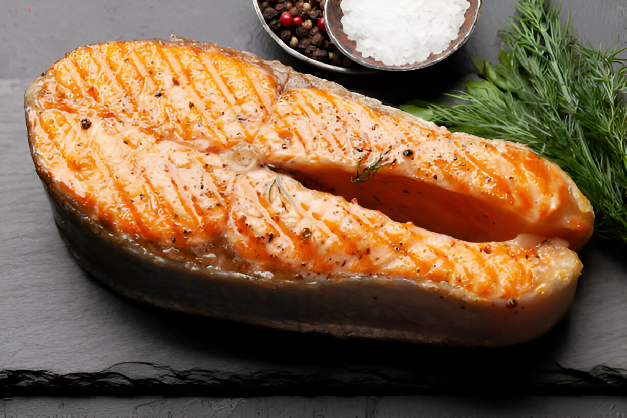 Cooked salmon steak garnished with herbs and spices on a slate background.