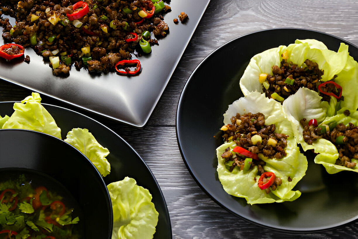 A delicious plate of lettuce wraps filled with seasoned minced meat, garnished with red chilies and green onions, served with a side of fresh lettuce and broth.