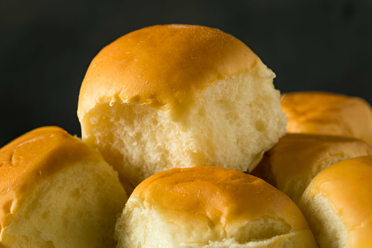 Fluffy golden dinner rolls stacked together with one partially broken open